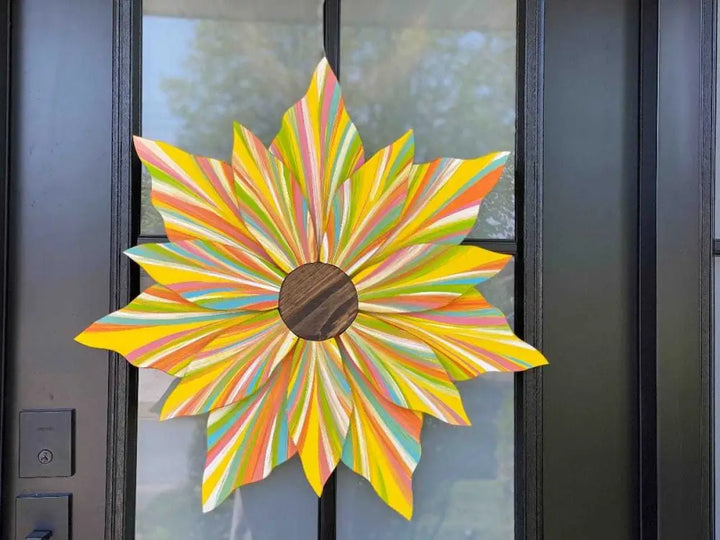 Colorful handcrafted wooden flower door decoration with striped petals and wooden center hanging on black door