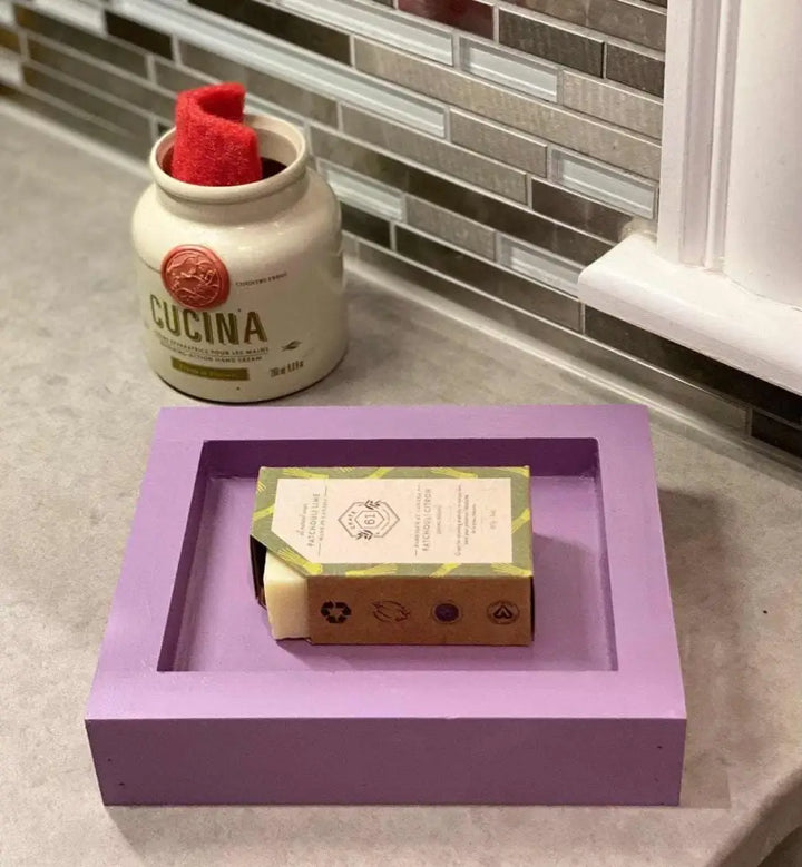 Handcrafted pine soap dish in purple with bar soap on kitchen counter.