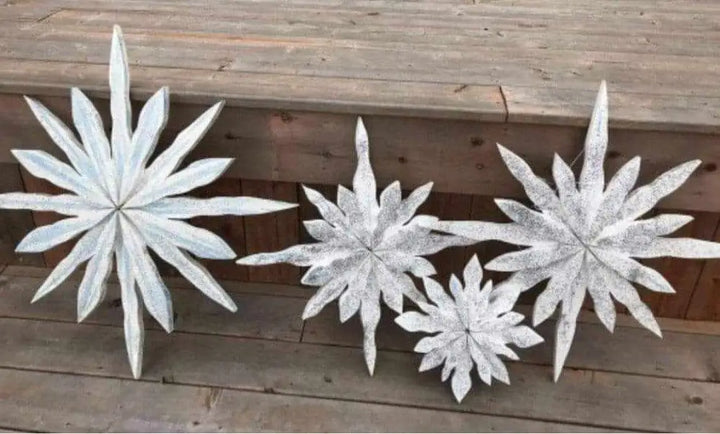 Handcrafted snowflake decorations with a maritime winter theme, lightly dusted in silver glitter, displayed on a wooden surface.