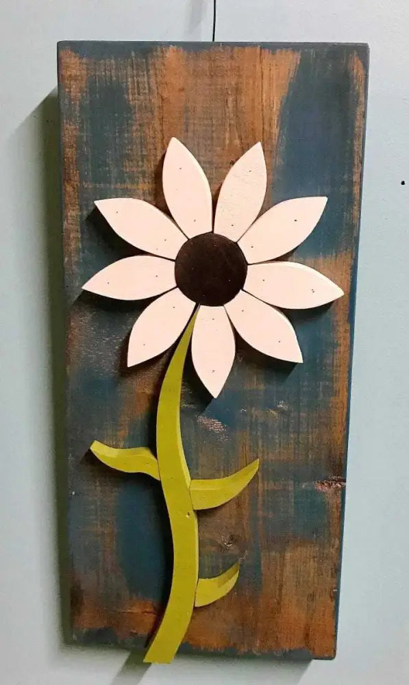 Handcrafted wooden wall art flower with white petals and green stem on rustic brown and blue background