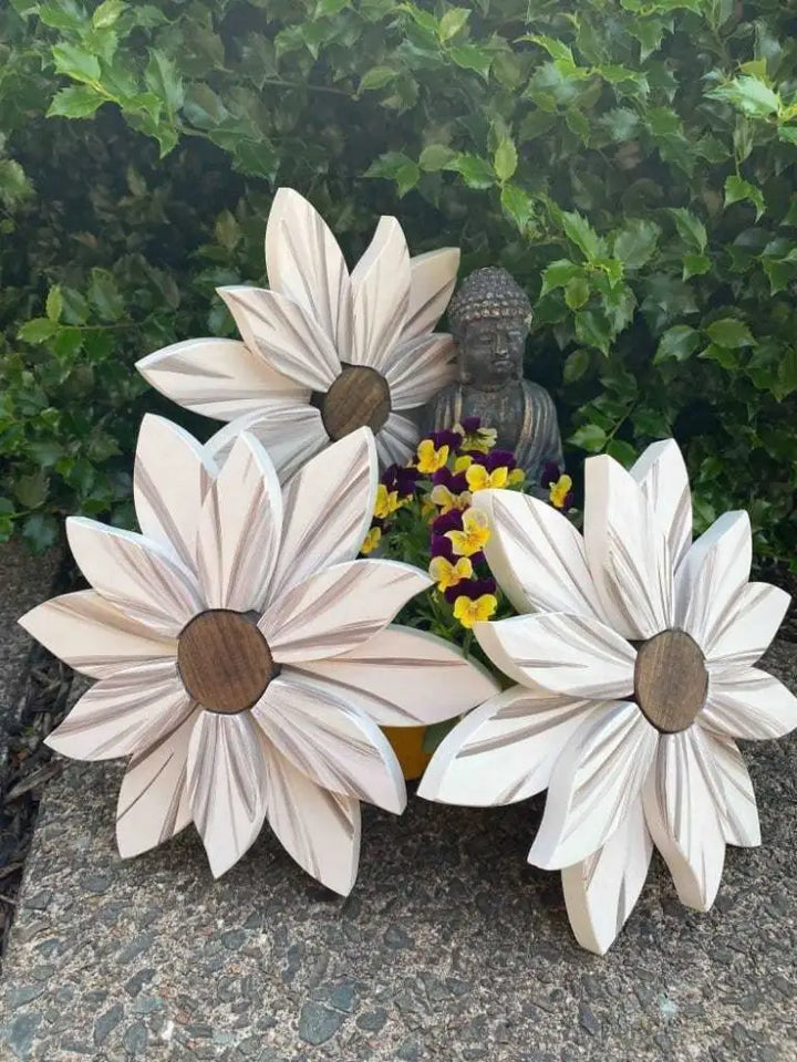 Wooden flower art pieces with lifelike petals and stained wooden centers displayed outdoors.