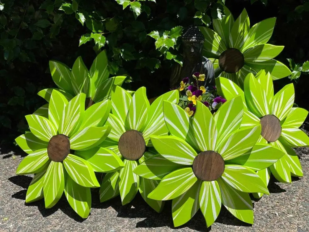 Wooden flower art pieces in vibrant green with brown centers, displayed outdoors amidst greenery.