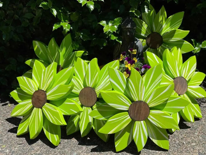 Wooden flower art pieces in vibrant green with brown centers, displayed outdoors amidst greenery.