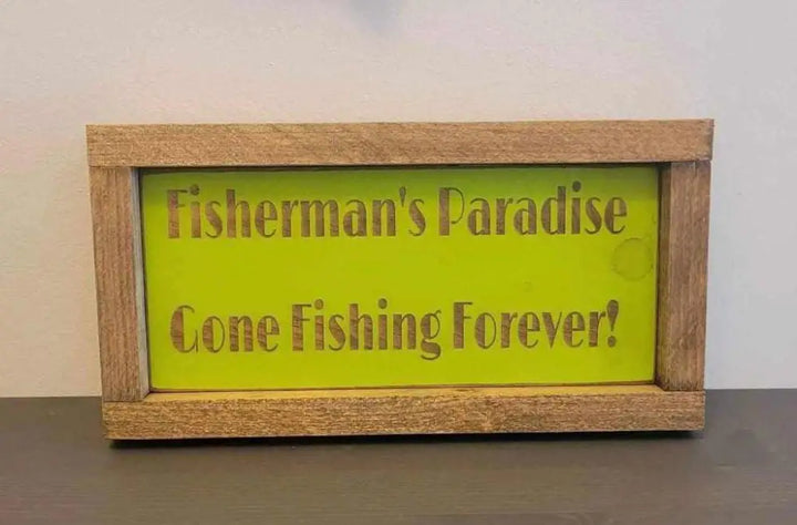 Laser engraved wood sign with "Fisherman's Paradise, Gone Fishing Forever" text, perfect for outdoor enthusiasts.