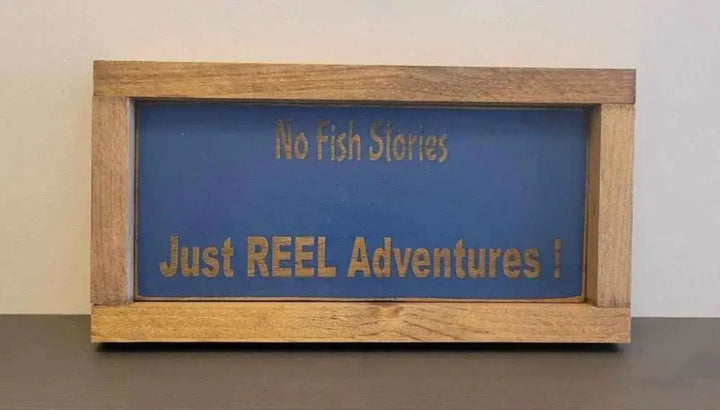 Laser engraved wood sign with "No Fish Stories, Just REEL Adventures" in rustic frame. Ideal for outdoor enthusiasts.