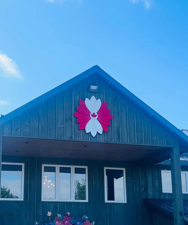 Large handcrafted wooden flower decoration painted red and white mounted on a dark blue building facade under a clear sky