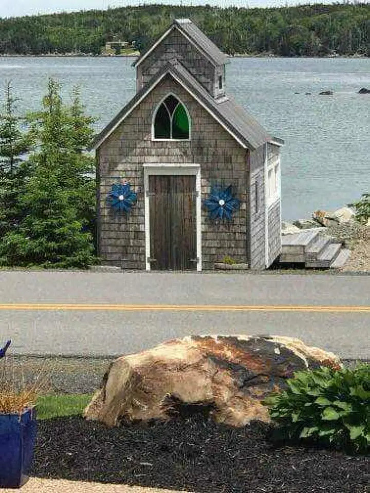Handcrafted wooden flower art on a rustic shed by a lake.
