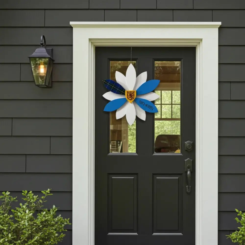 Decorative door wreath with blue and white flowers on a black door with gray siding.