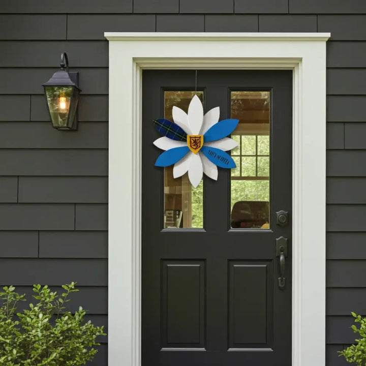 Decorative door wreath with blue and white flowers on a black door with gray siding.