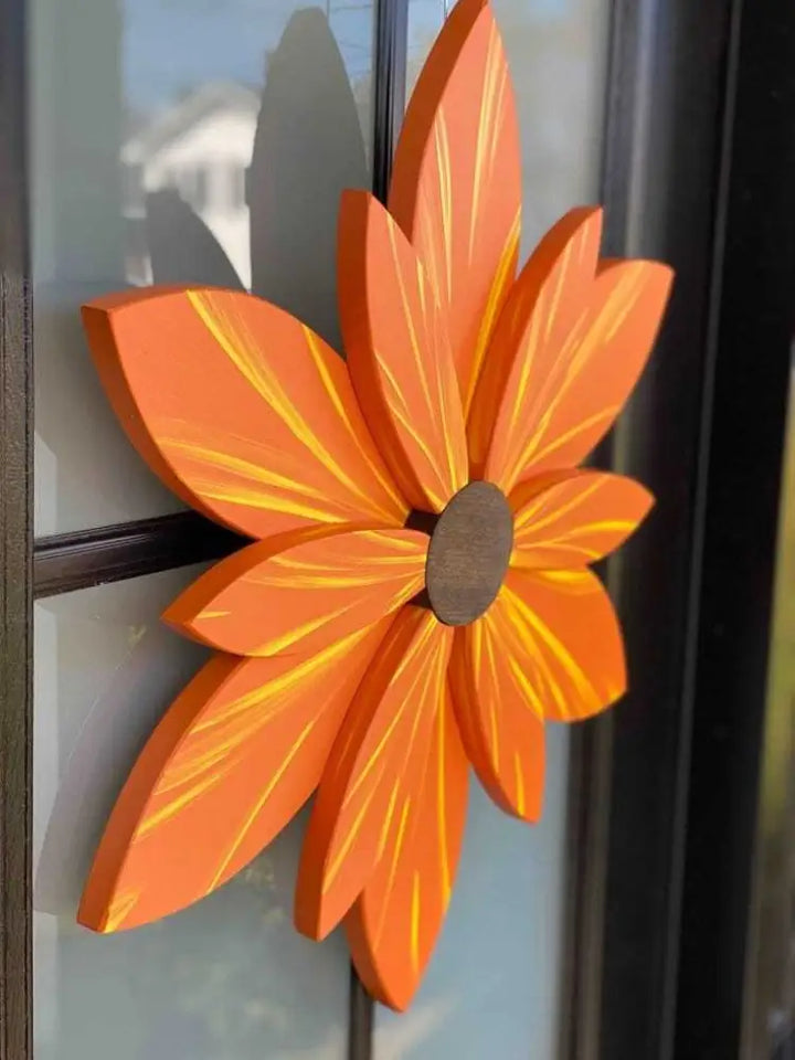 Handcrafted orange and yellow wood flower door decoration hanging outdoors.