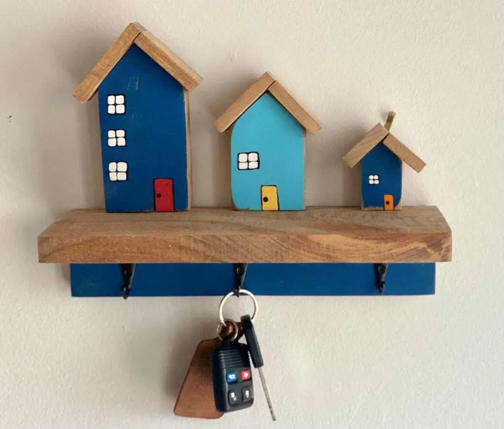Wall-mounted key chain holder with three house-shaped hooks, holding keys.