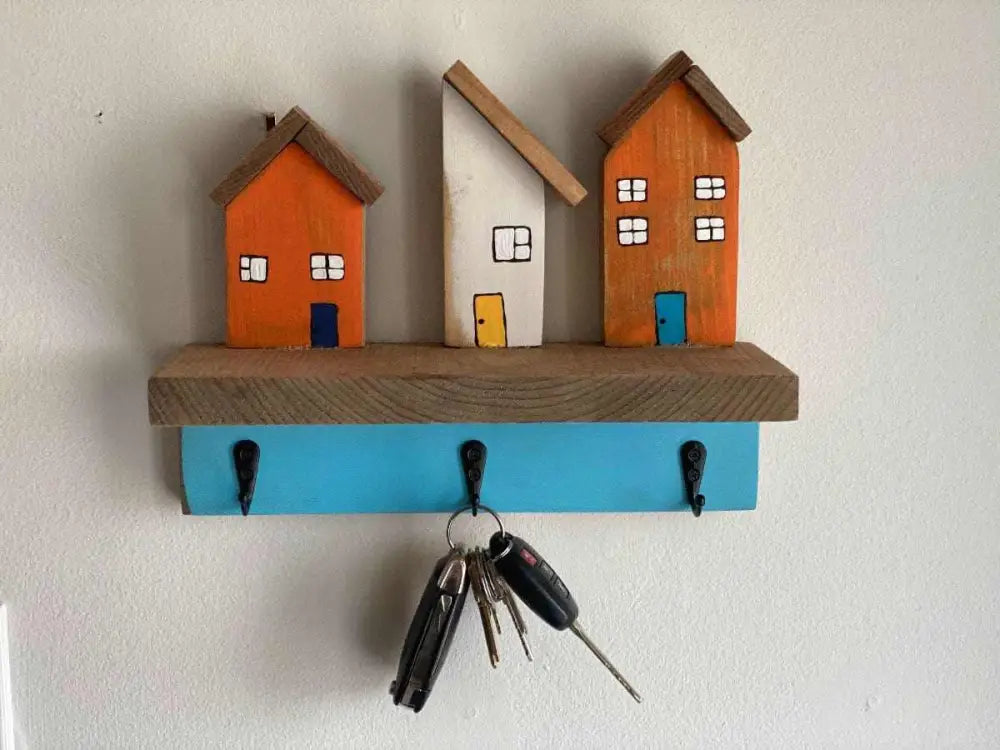 Wall mounted key chain holder with three colorful house designs and hooks.