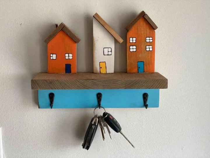 Wall mounted key chain holder with three colorful house designs and hooks.