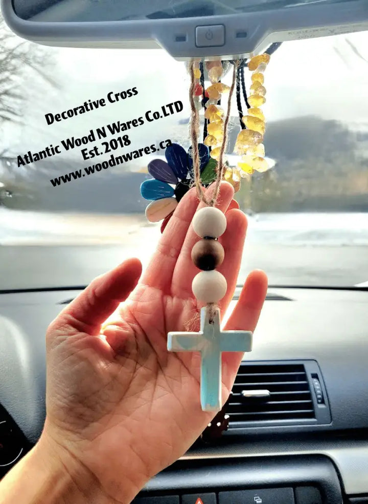 Hand holding a rustic wooden bead and cross garland, used as decorative car hanging.