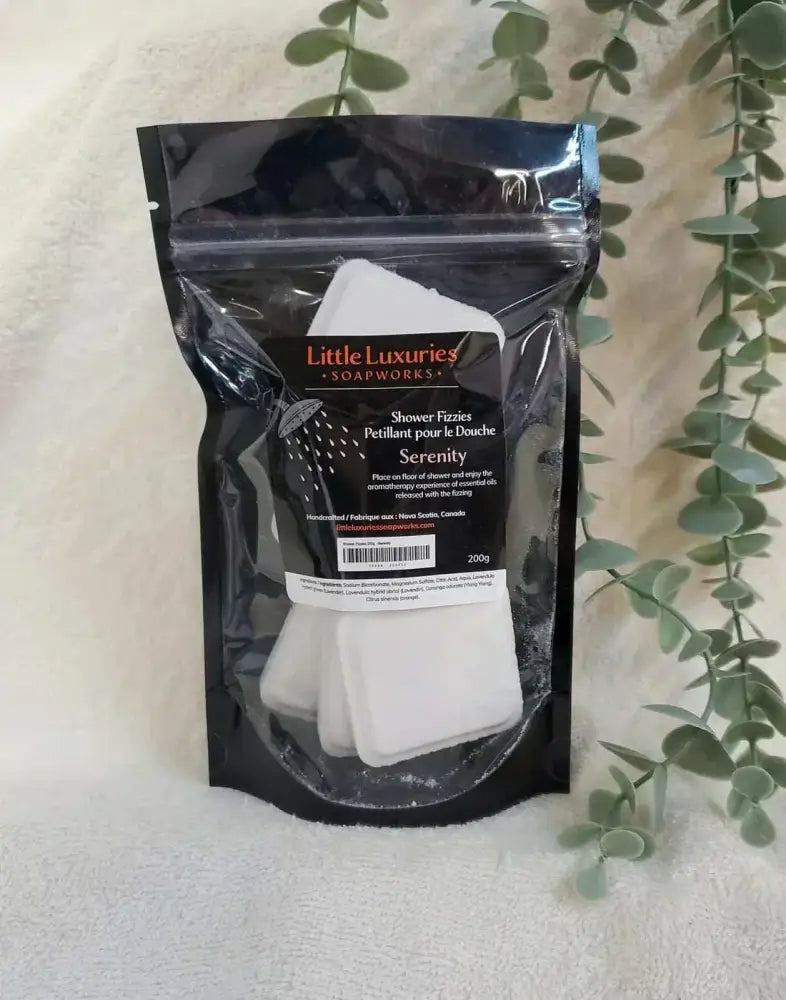 Pack of Little Luxuries Soapworks Serenity Shower Steamers with essential oils in resealable black pouch beside eucalyptus leaves