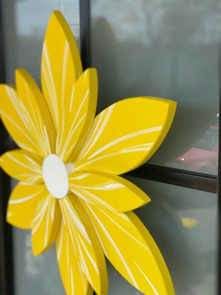 Yellow wooden flower decor with hand-painted petals displayed on window.