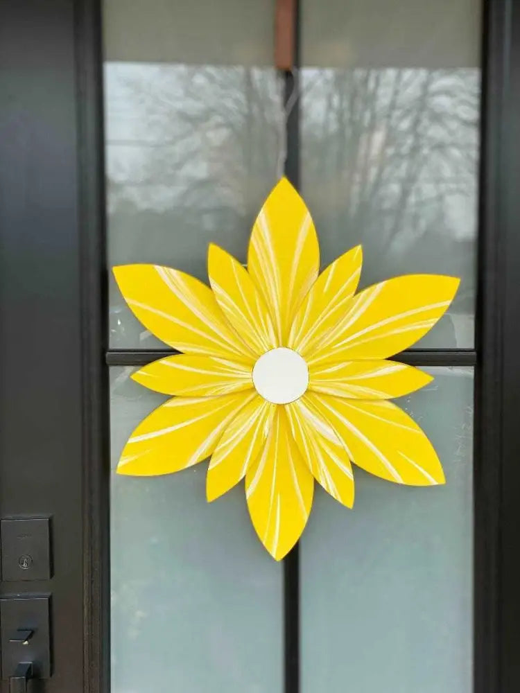 Bright yellow wooden flower decoration on a door, handcrafted and painted for long-lasting beauty and protection.