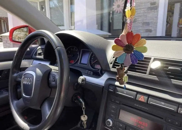 Colorful Sofia Daisy clay charm with black lava bead hanging from car rearview mirror inside Audi vehicle interior
