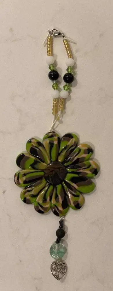 Hand-sculpted Sofia Daisy Car/Window Charm with green petals, black lava bead, and glass beads, supporting IWK Foundation.