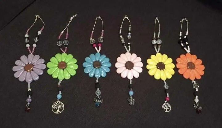 Colorful Sofia Daisy hand-sculpted polymer clay car and window charms with beads and elastic cords arranged on a dark background