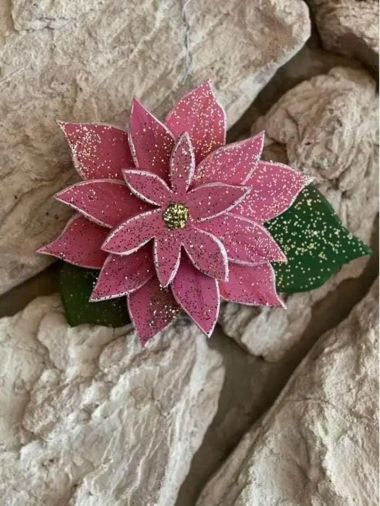 Wooden flower poinsettia with pink petals on textured background, symbolizing holiday celebration.