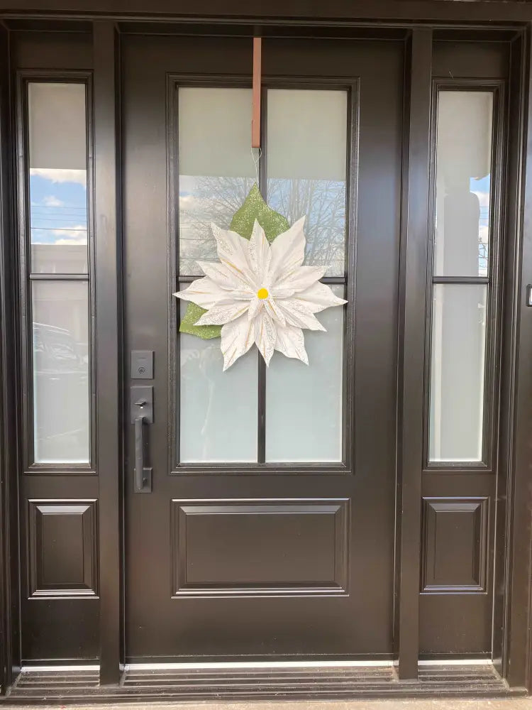 Wooden Poinsettia flower decoration hanging on a black front door, symbolizing holiday cheer.