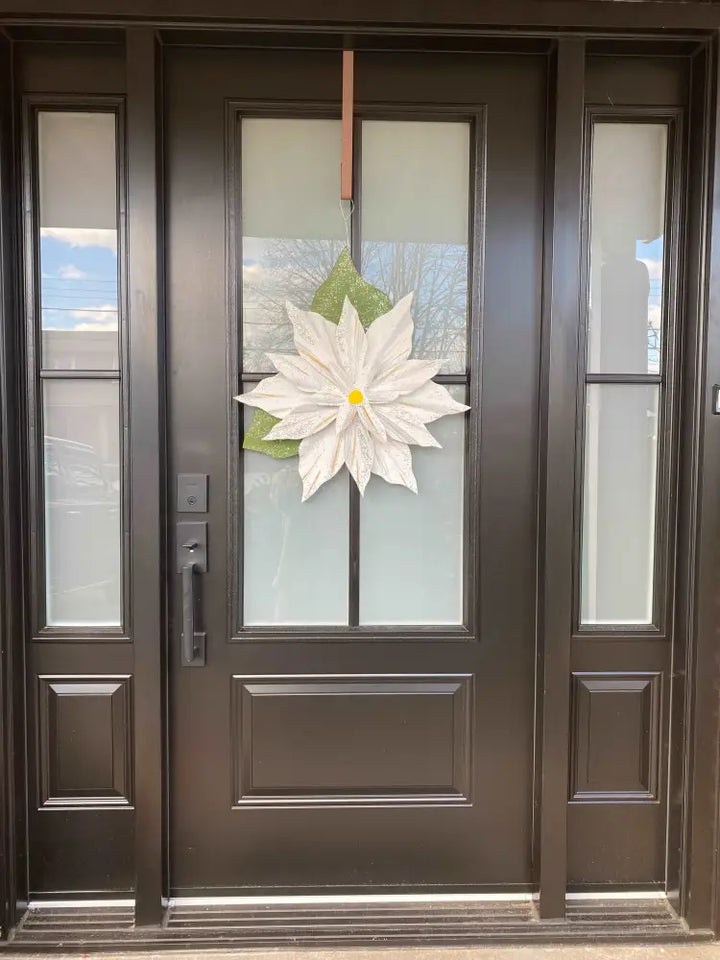 Wooden Poinsettia flower decoration hanging on a black front door, symbolizing holiday cheer.