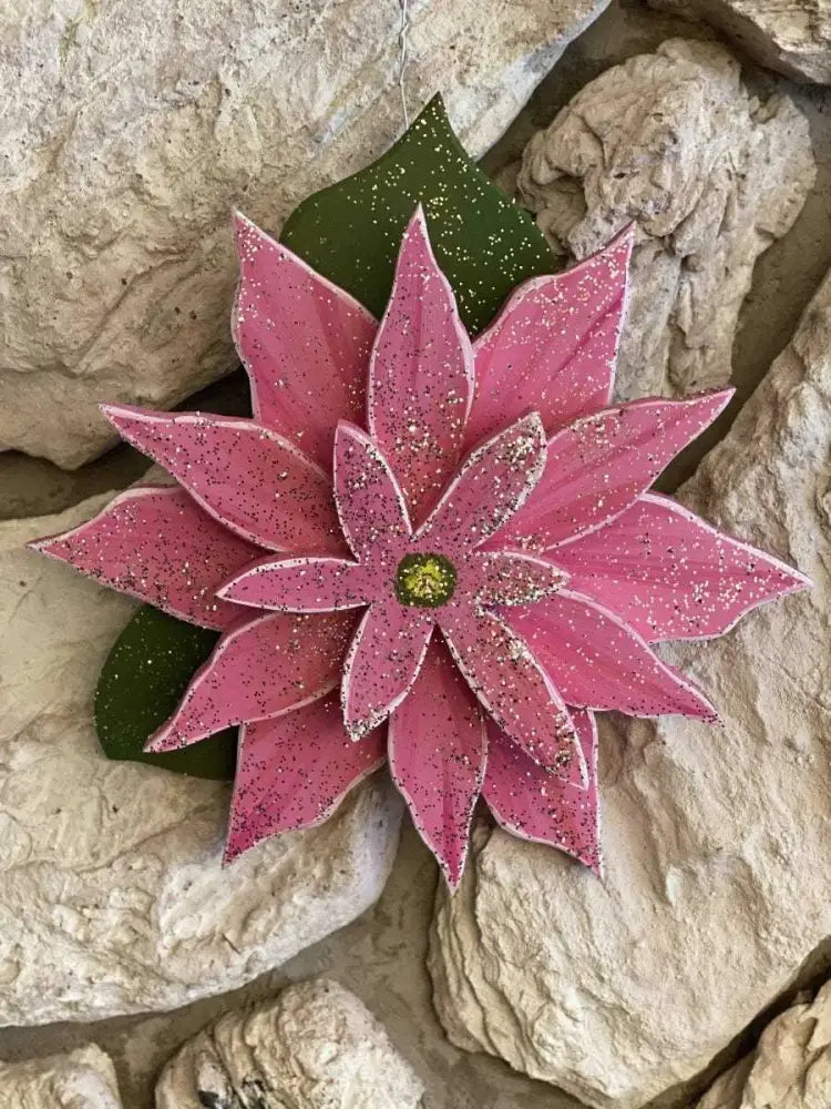 Wooden pink poinsettia decoration on rocks, symbolizing joy and celebration for the holiday season.