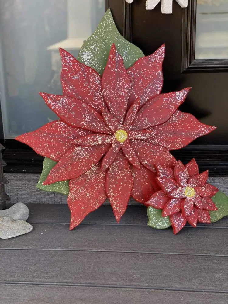 Wooden poinsettia flowers with red petals symbolizing blessings, on a background with green leaves, available in various sizes for holiday decoration.