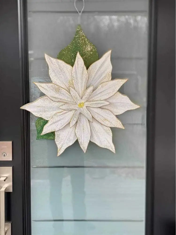 Wooden poinsettia flower decoration with white petals hanging on a door.