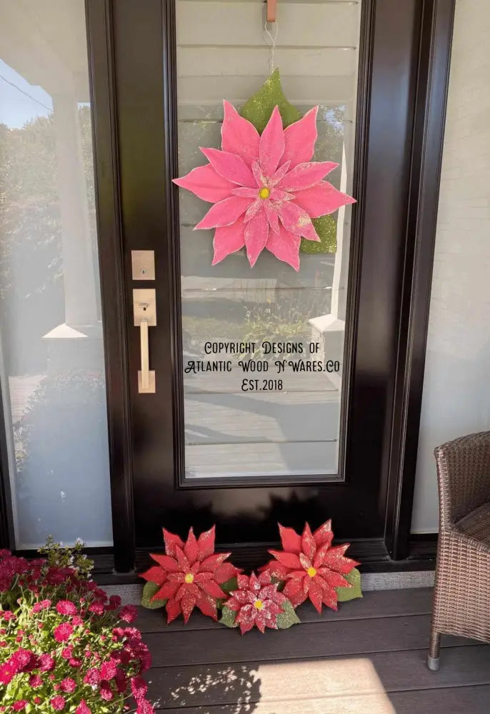 Wooden poinsettia decorations on a front door and porch, symbolizing Christmas themes with vibrant red leaves.