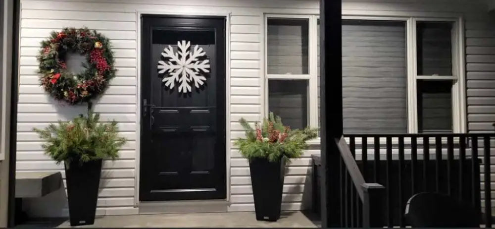 Handmade snowflake decoration on door with festive wreath and winter plants.