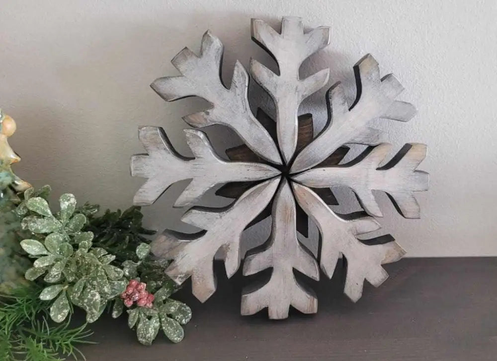 Handmade wooden snowflake decoration with a rustic finish, next to greenery, ideal for winter door decor.