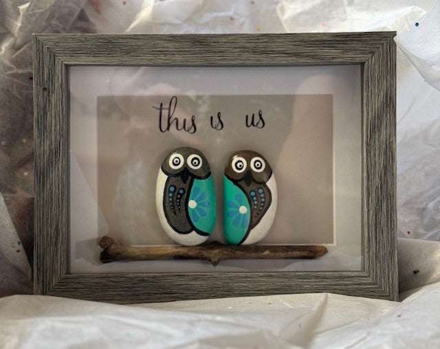 Handmade pebble art featuring owl couple on a branch in grey frame.