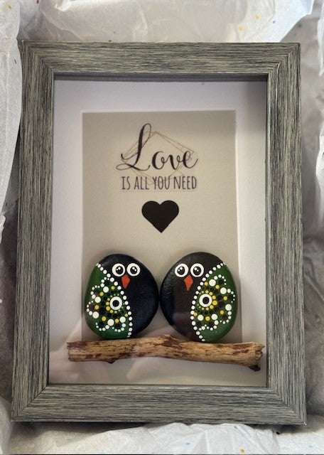 Handmade pebble art with owl couple on branch in grey frame.