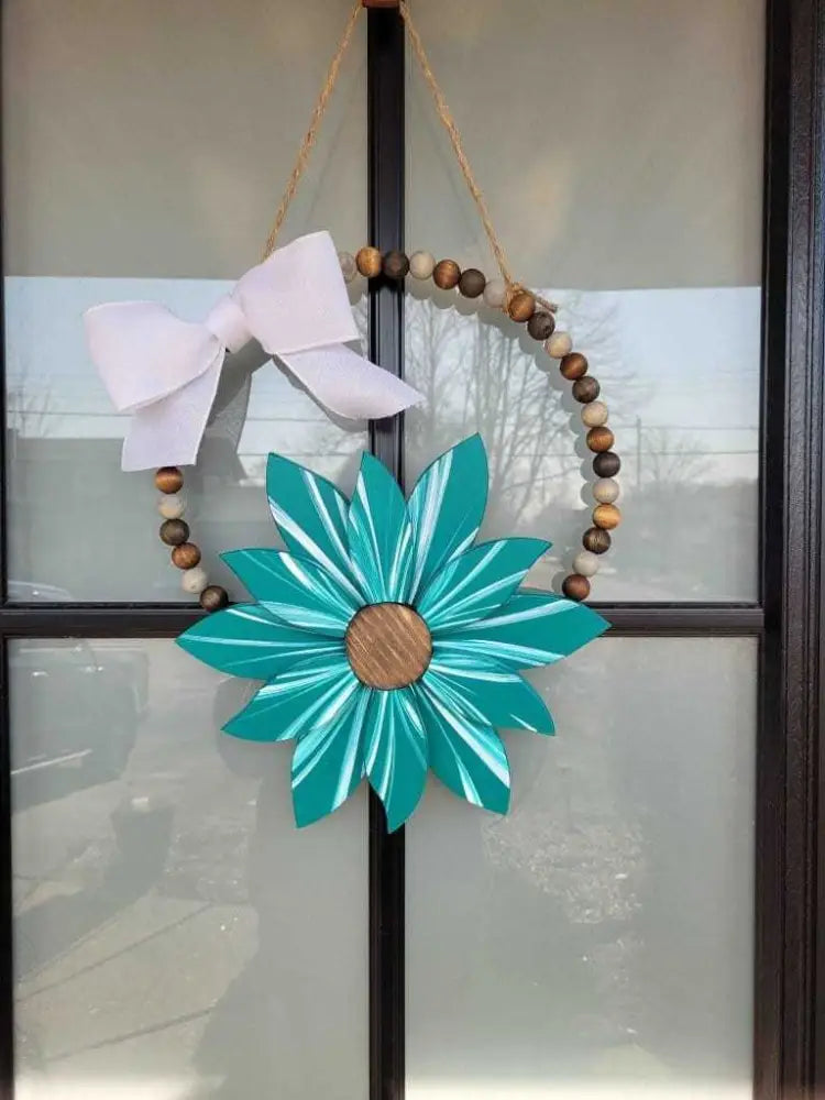 Boho style wooden bead wreath with a large painted turquoise flower and white bow.
