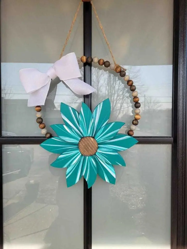 Boho style wooden bead wreath with a large painted turquoise flower and white bow.