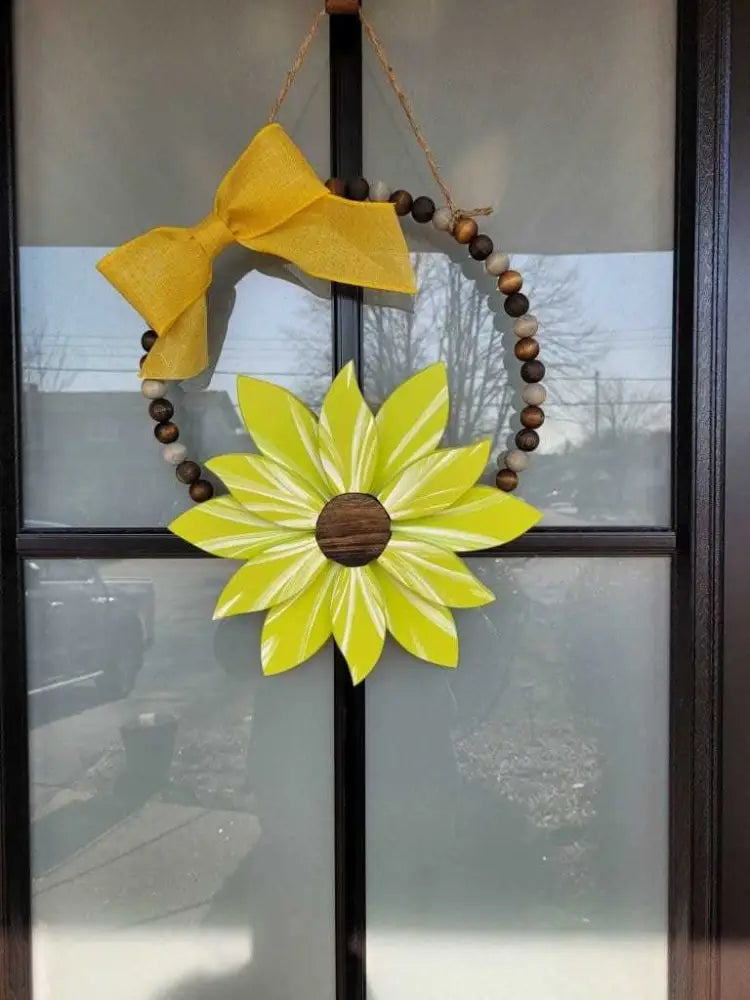 Boho style wooden bead wreath with painted wood flower and yellow bow, hanging on a door.
